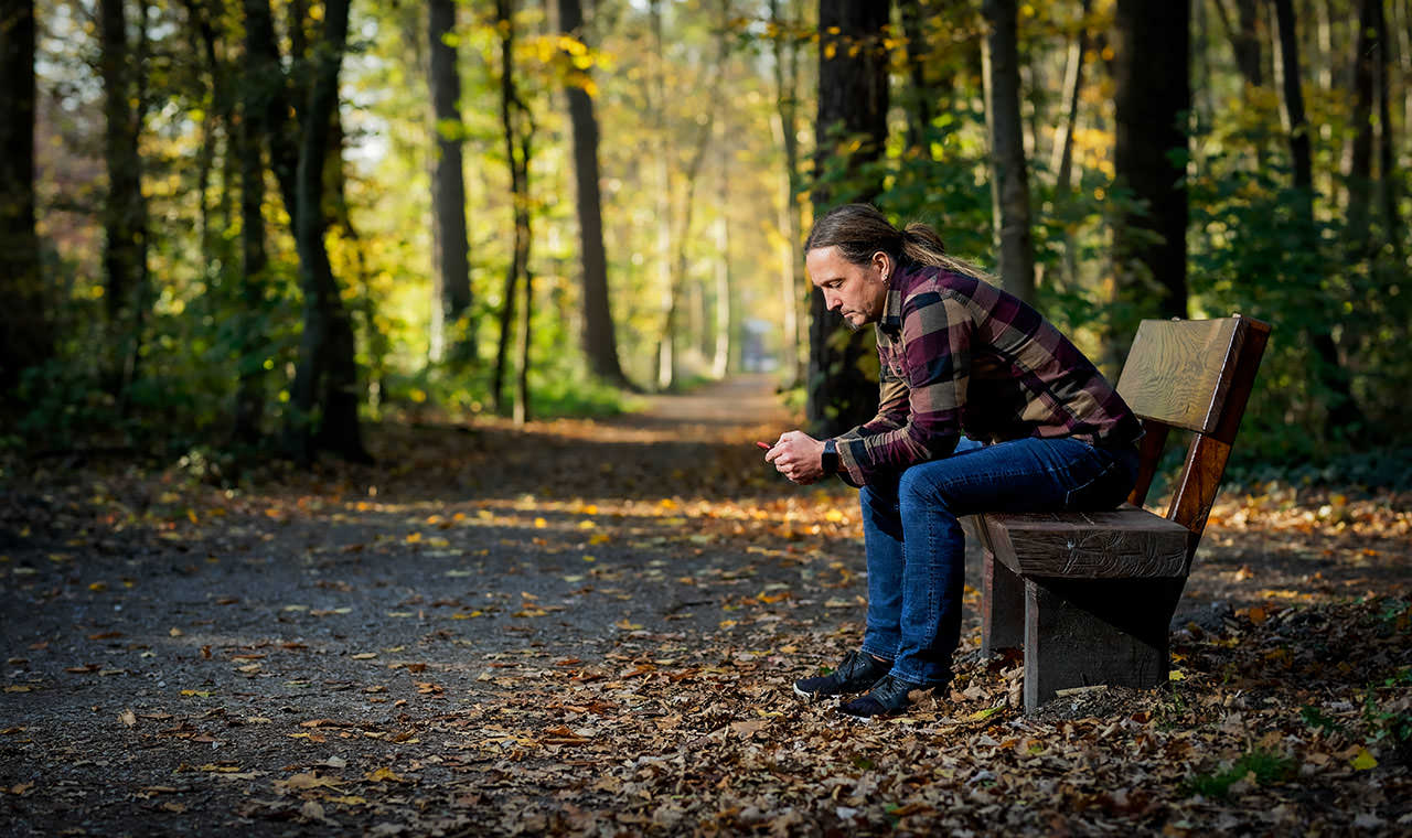 Ein Foto auf dem ich im Wal auf einer Bank sitze und auf mein Mobiltelefon schaue