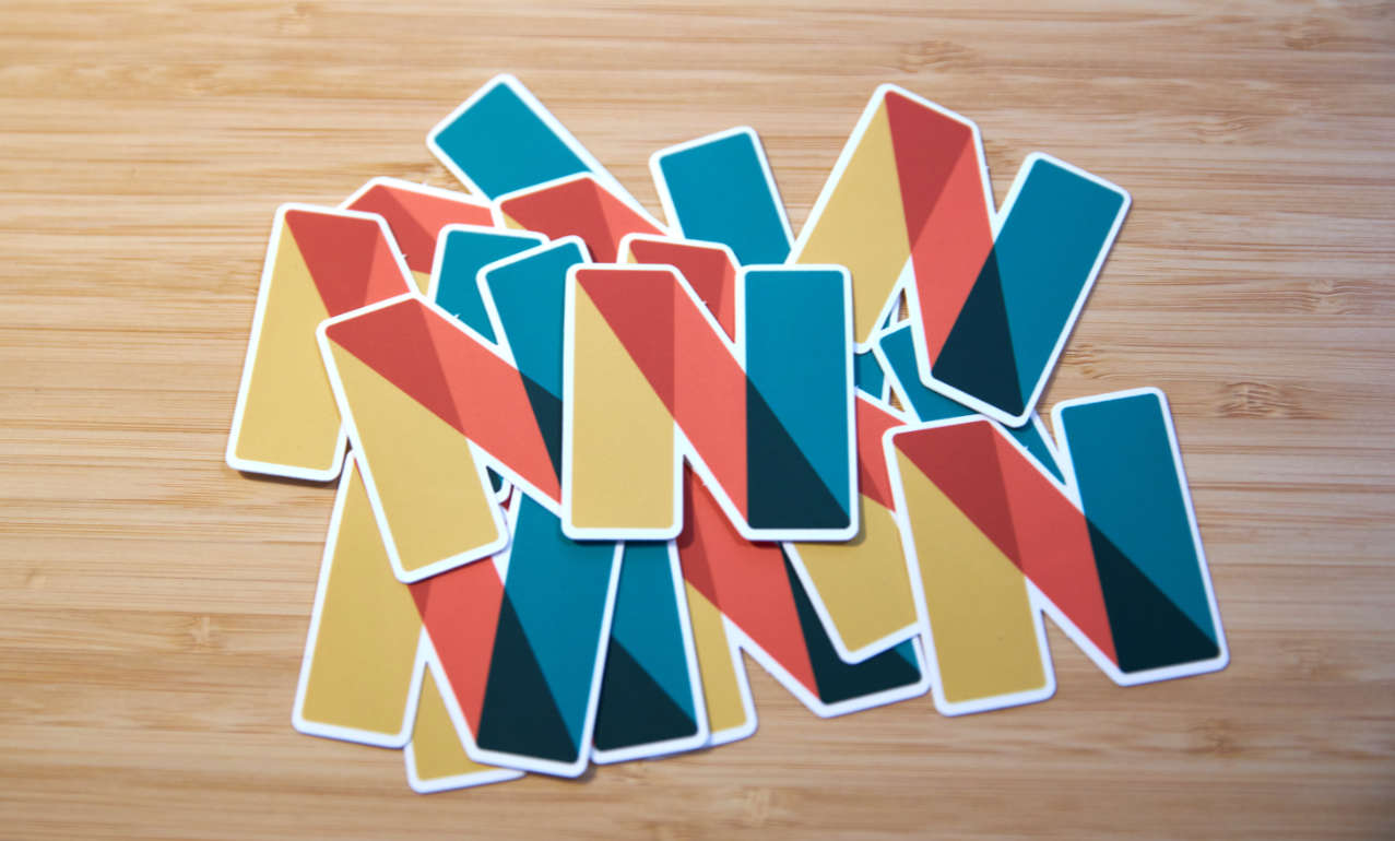 Auf dem Foto sieht man einen Haufen bunte Sticker, die auf einem Holzuntergrund liegen. Die Sticker sind gelb, rot und grün und zeigen ein N.